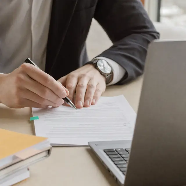 A lawyer's hands marking up a printed document next to a laptop